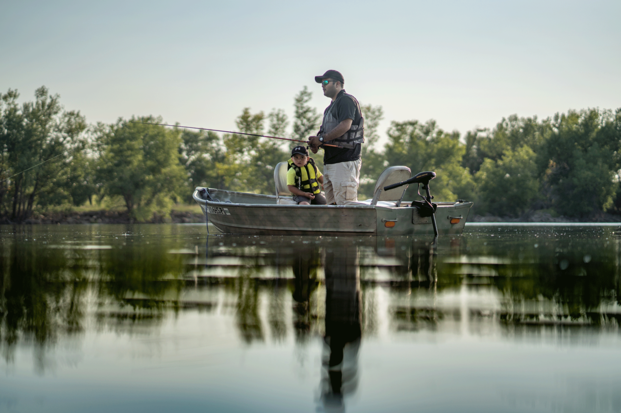 A father and son fishing from a boat on open water.