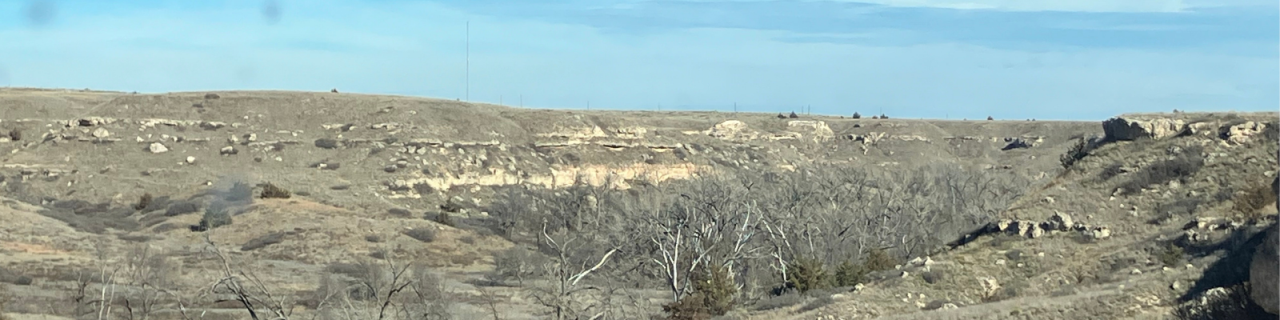 Rocky canyon-like terrain with sparse trees and layered hills stretches beneath a wide sky.