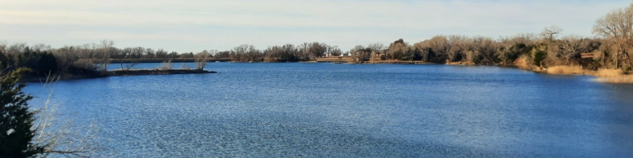 A wide, calm lake stretches across the landscape with tree-lined shores and a clear sky above.
